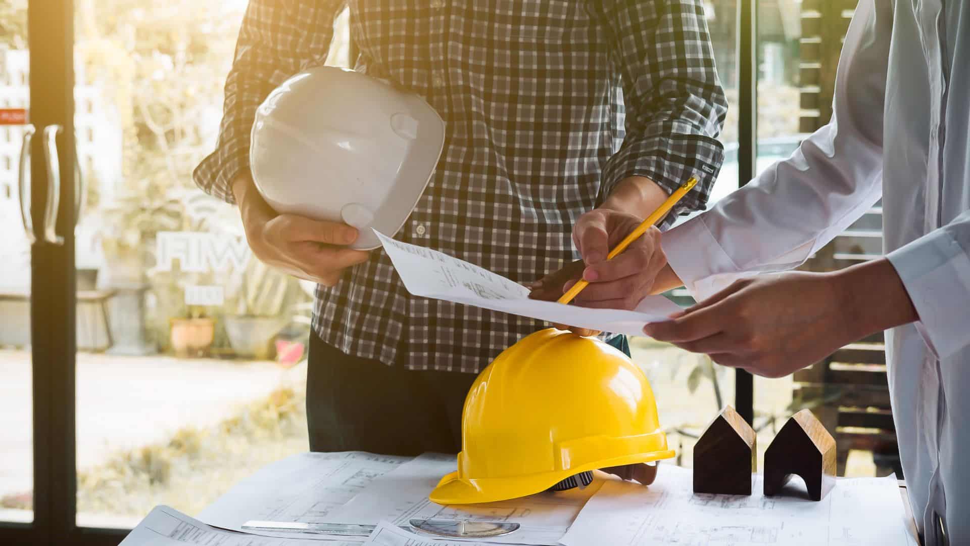 Jak znaleźć pracę za granicą – pracownicy omawiający dokumenty i plany budowlane z kaskami ochronnymi