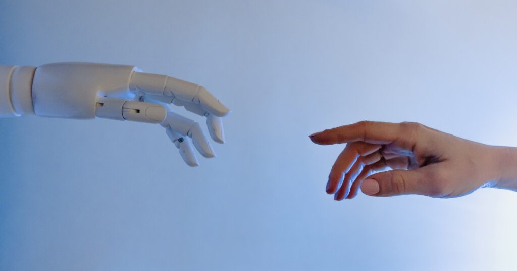 Robotyczna i ludzka dłoń zbliżające się do siebie – symbol relacji człowieka i sztucznej inteligencji