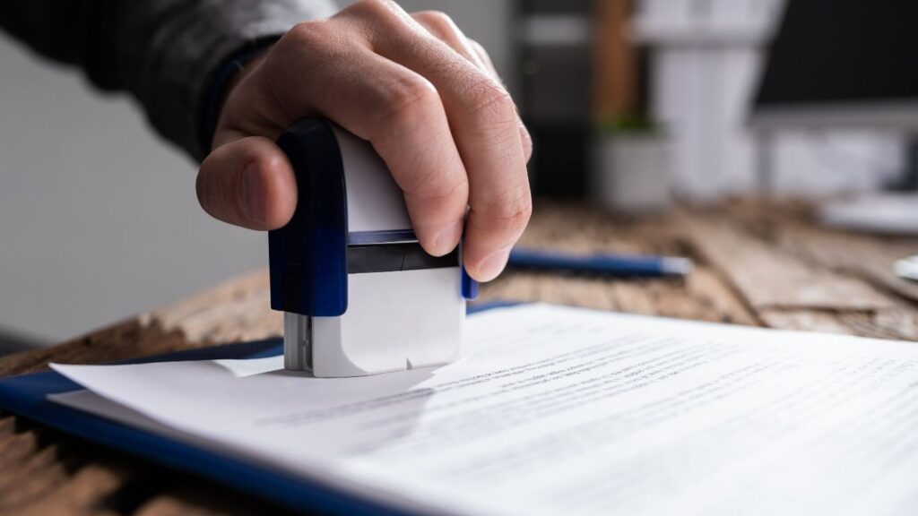Ręka przybijająca pieczątkę na dokumencie – oświadczenie o powierzeniu pracy: kiedy ma sens, limity i ryzyka.
